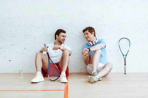 Squash player sitting on floor and showing smartwatch to friend — Stock Photo