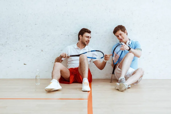 Squash players sitting on floor and looking at racket — Stock Photo