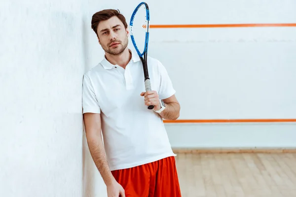 Barbudo jugador de squash sosteniendo raqueta y mirando a la cámara - foto de stock