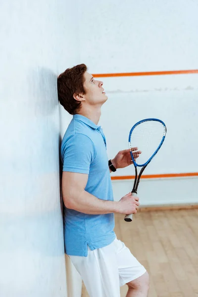 Vue latérale du triste joueur de squash tenant la raquette dans un court à quatre murs — Photo de stock