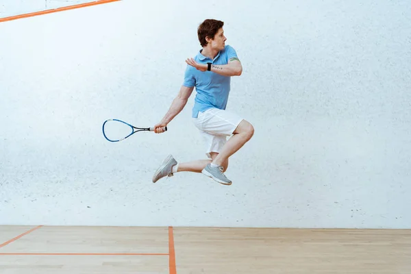 Sportsman in polo shirt jumping while playing squash in four-walled court — Stock Photo
