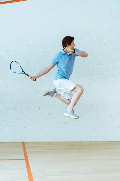 Спортсмен в футболке для поло прыгает во время игры в сквош в четырехстенном корте — стоковое фото