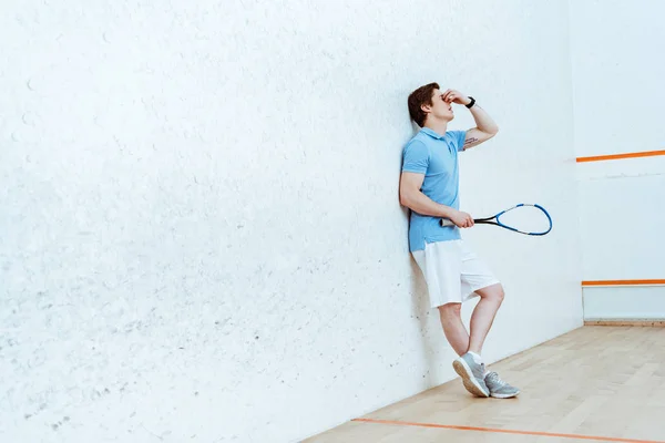 Vista completa del jugador de squash cansado tocando los ojos con la mano - foto de stock