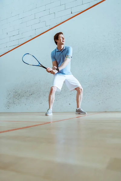 Visão de comprimento total do esportista concentrado em camisa de pólo azul jogando squash — Fotografia de Stock