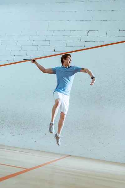 Full length view of excited sportsman in blue polo shirt jumping while playing squash — Stock Photo