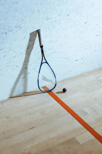 Uma raquete de squash e bola no chão de madeira em quadra de quatro paredes — Fotografia de Stock