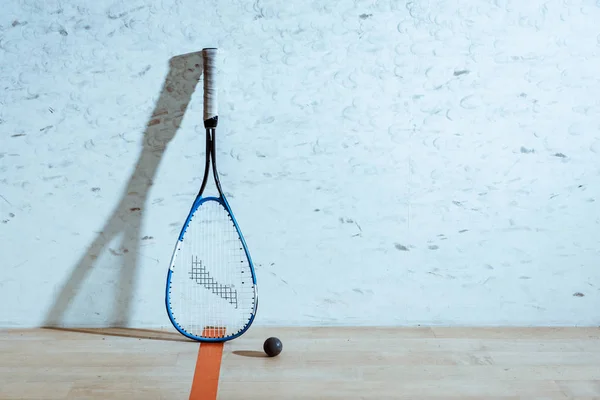 One squash racket and ball on wooden floor in four-walled court — Stock Photo