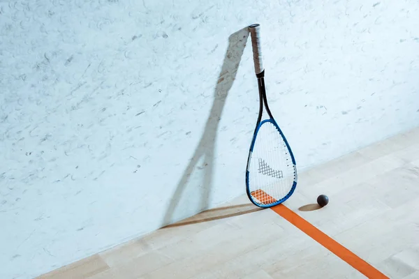 Squash racket and ball on wooden floor in four-walled court — Stock Photo