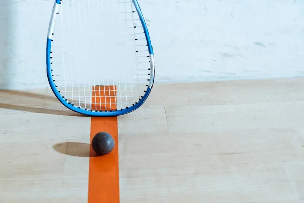 Squash raquete e bola no chão de madeira em quadra de quatro paredes — Fotografia de Stock