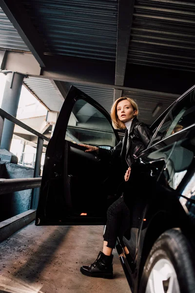 Jolie fille blonde debout près de voiture noire avec porte ouverte — Photo de stock