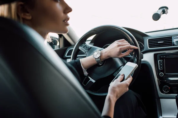Corte vista de mulher loira sentado no carro e segurando smartphone — Fotografia de Stock