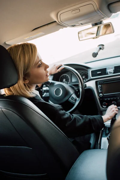 Mujer joven rubia sosteniendo la manija del cambio de marcha mientras está sentado en el coche - foto de stock