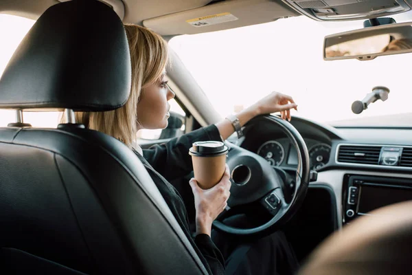 Blonde young woman holding paper cup while sitting in car — Stock Photo