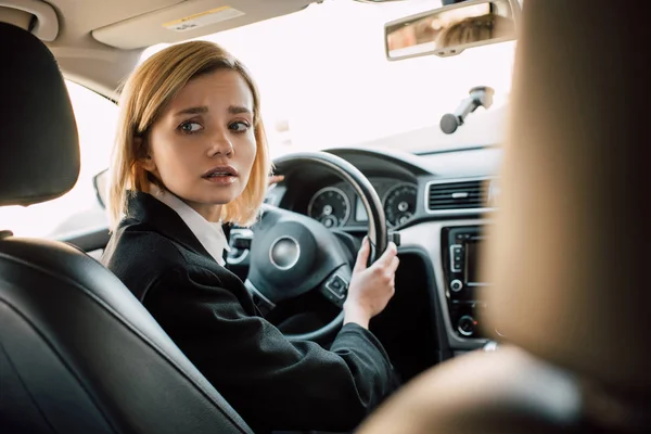 Preoccupato donna bionda che tiene il volante mentre seduto in auto — Foto stock