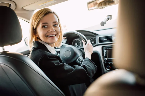 Mujer rubia feliz sosteniendo el volante mientras está sentado en el coche - foto de stock