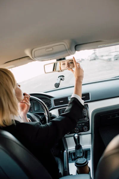 Вид сзади блондинки, прикасающейся к зеркалу, сидя в машине — стоковое фото