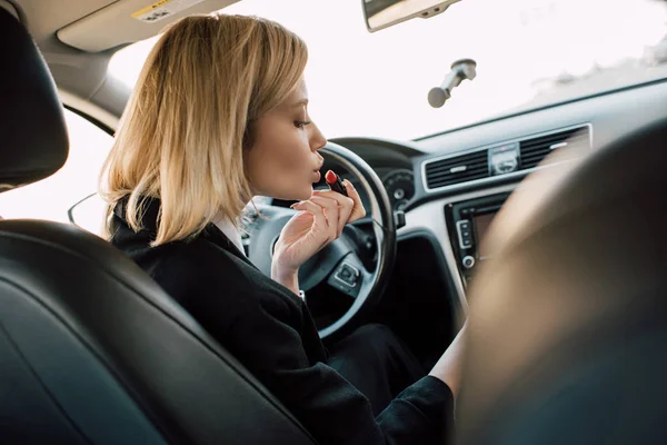 Attraktives blondes Mädchen trägt Lippenstift auf, während es im Auto sitzt — Stockfoto