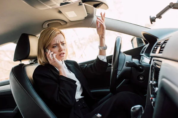 Molesto joven rubia hablando teléfono inteligente mientras está sentado en el coche - foto de stock