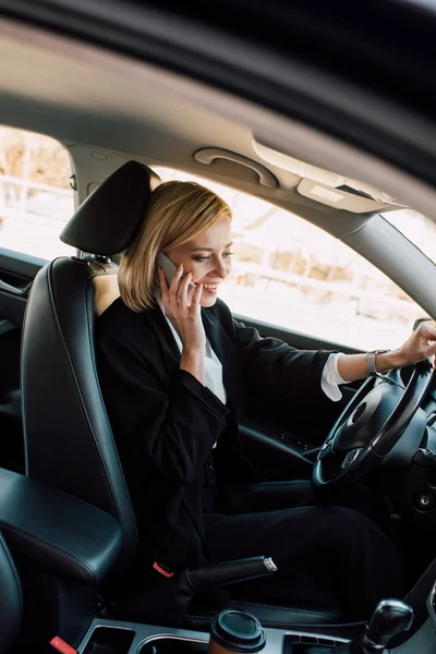 Cheerful blonde young woman talking on smartphone while driving car — Stock Photo