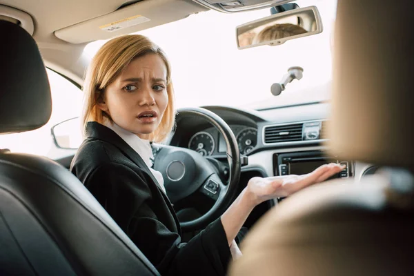 Stressed blonde young woman gesturing while sitting in car — Stock Photo