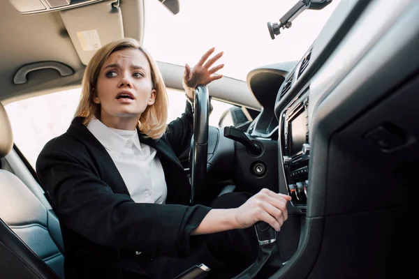 Vista de ángulo bajo de la mujer rubia emocional gesto mientras está sentado en el coche - foto de stock