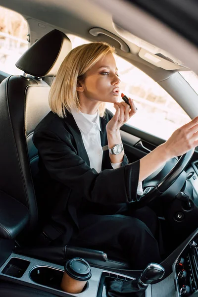 Schöne blonde junge Frau, die Lippenstift aufträgt, während sie im Auto sitzt — Stockfoto