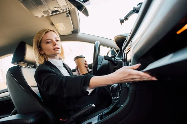Low angle view of attractive blonde woman holding coffee to go in car — Stock Photo