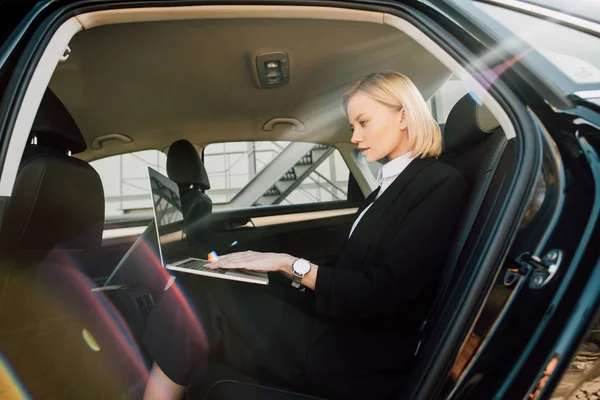 Attraktive blonde Frau benutzt Laptop während sie im Auto sitzt — Stockfoto