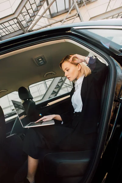Красива блондинка молода жінка використовує ноутбук, сидячи в машині — стокове фото