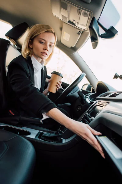 Низкий угол обзора привлекательной блондинки, держащей кофе, чтобы поехать в машине — стоковое фото