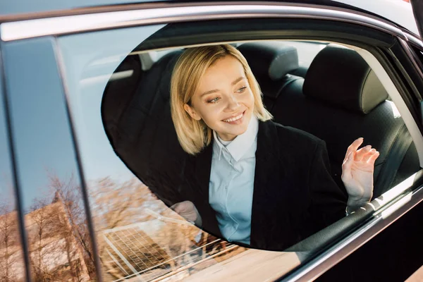 Joyeuse jeune femme blonde assise et souriante dans l'automobile — Photo de stock