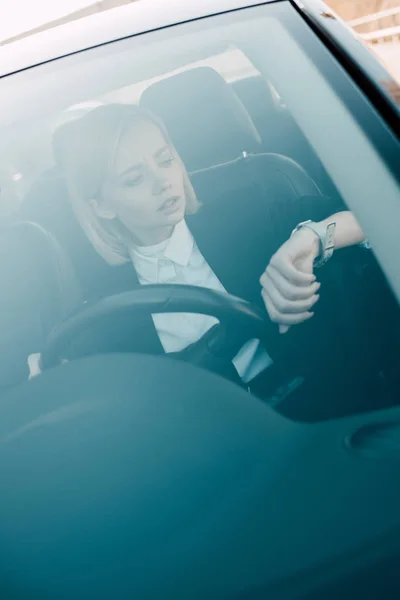 Attractive blonde driver looking at watch while holding steering wheel — Stock Photo