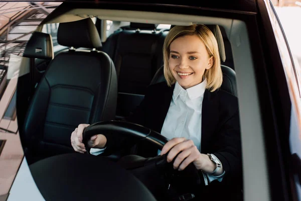 Cheerful blonde driver holding steering wheel while driving car — Stock Photo