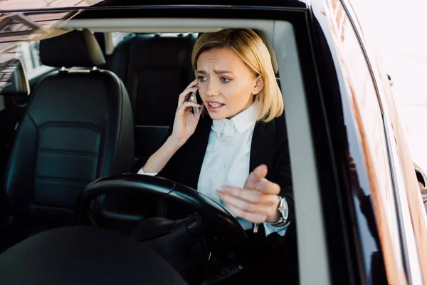 Chateado mulher loira falando no smartphone enquanto gestos no carro — Fotografia de Stock