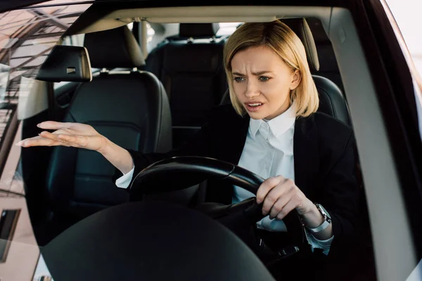 Virado menina loira segurando volante enquanto gesticulando e carro de condução — Fotografia de Stock