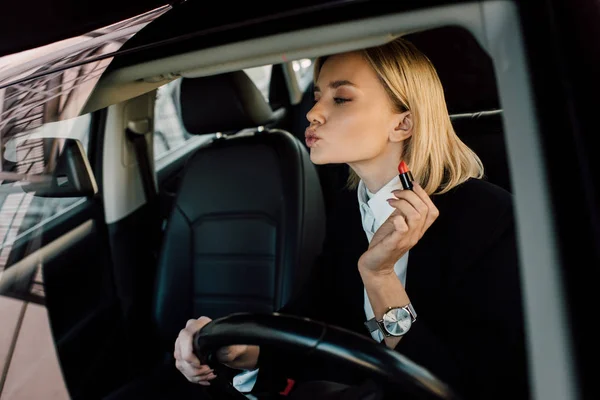 Jolie femme blonde avec le visage de canard tenant rouge à lèvres dans la voiture — Photo de stock