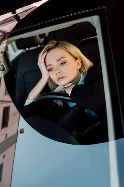 Mujer joven rubia molesta sentada en un automóvil moderno - foto de stock
