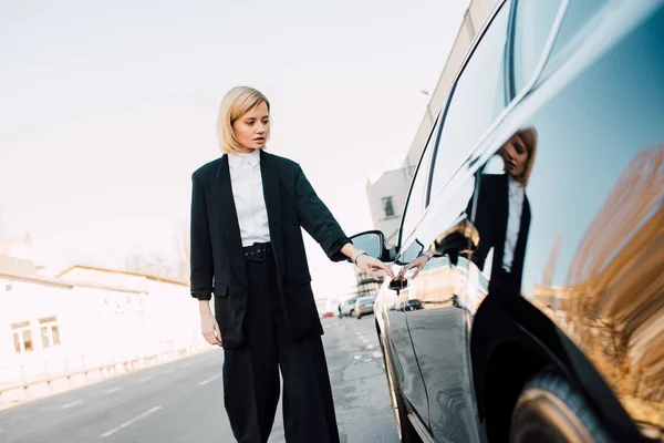Schöne blonde Frau steht neben schwarzem Auto auf Parkplatz — Stockfoto