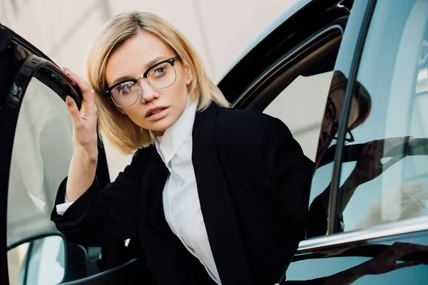 Bela loira jovem mulher em óculos perto de automóvel preto — Fotografia de Stock