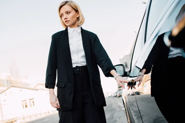 Stylish blonde young woman standing near black car in parking — Stock Photo