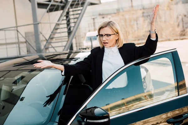 Frustrado joven mujer gesto cerca de coche negro en el aparcamiento — Stock Photo