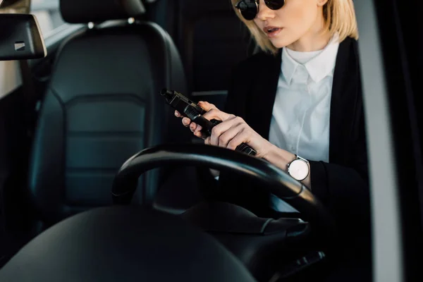Cropped view of blonde girl in sunglasses holding gun in car — Stock Photo