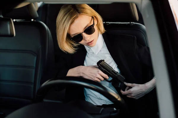 Mulher loira perigosa em óculos de sol segurando arma no carro — Fotografia de Stock
