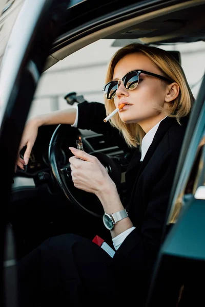 Blondine mit Sonnenbrille hält Feuerzeug beim Zigarettenrauchen im Auto — Stockfoto