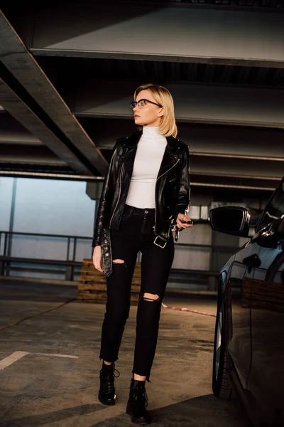 Blondine mit Brille hält Schlüssel auf Parkplatz in der Nähe von schwarzem Auto — Stockfoto