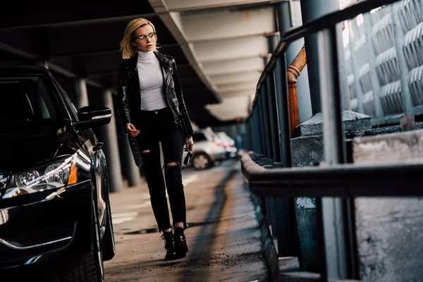 Schöne blonde Mädchen zu Fuß auf dem Parkplatz mit Schlüssel in der Nähe von schwarzen Auto — Stockfoto