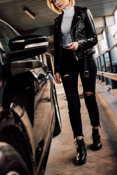 Вид блондинки, держащей ключ с брелоком рядом с черной машиной — стоковое фото