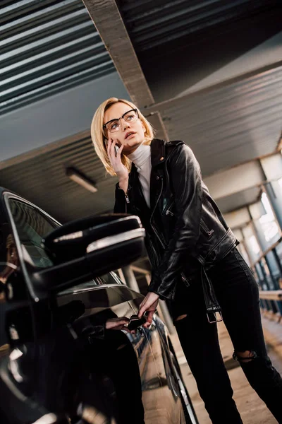 Blonde attractive girl talking smartphone while touching car door — Stock Photo