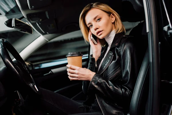 Blondes Mädchen hält Pappbecher in der Hand und spricht mit Smartphone im Auto — Stockfoto