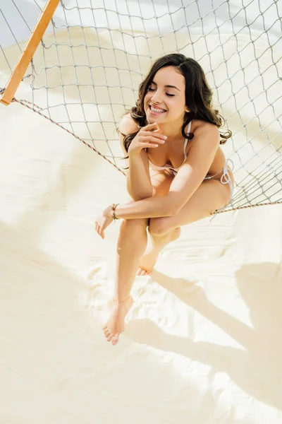 Hermosa chica sexy en bikini sonriendo y sentado en hamaca en la playa - foto de stock